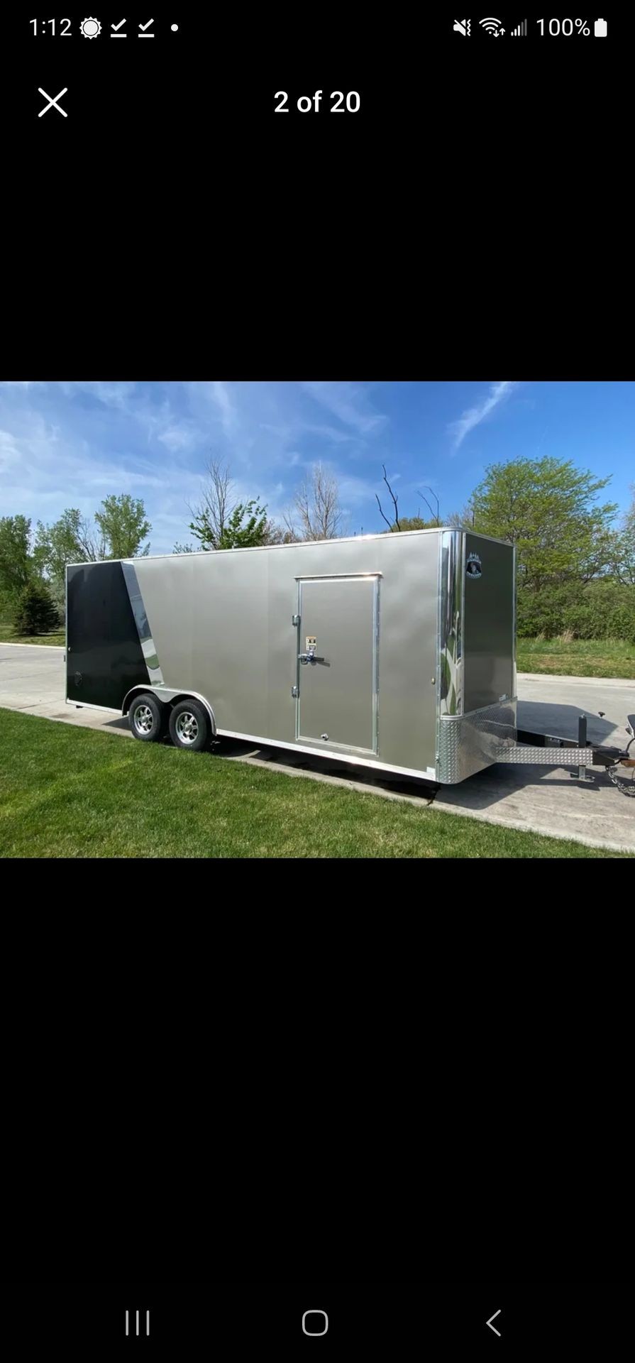 Silver and black enclosed trailer parked on a driveway with grass and trees in the background.